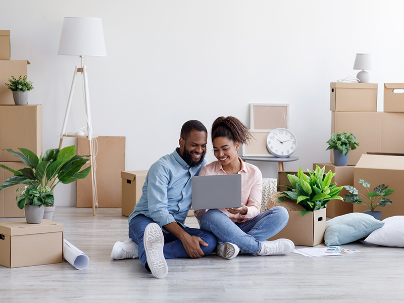 Black couple sitting on floor in living room surrounded by moving boxes