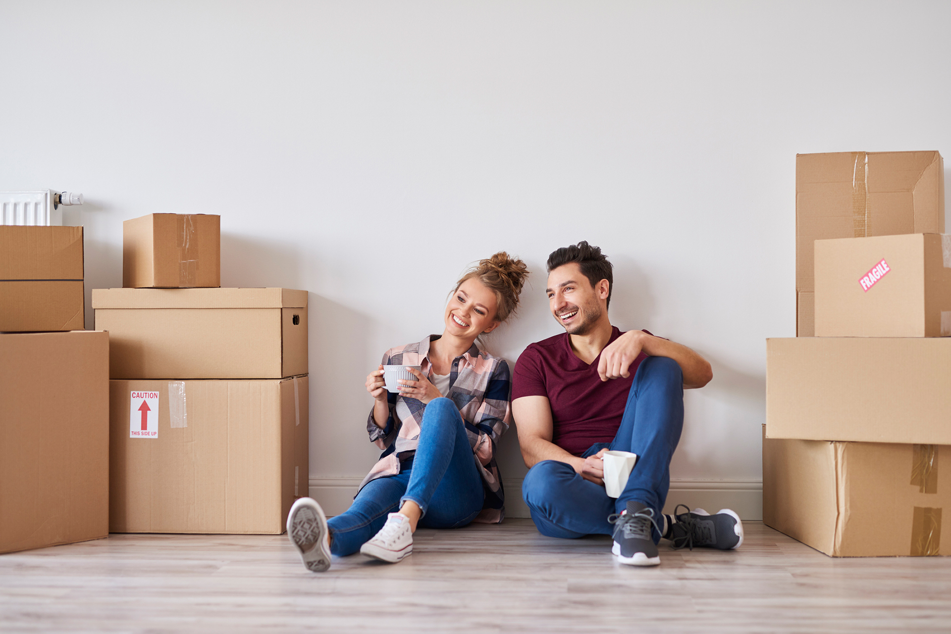 Couple sitting on the floor with moving boxes on either side of them. 